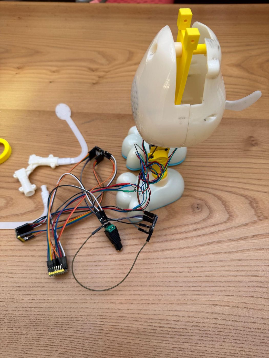 A 3D-printed white cat-shaped chassis with a yellow inner armature, standing on a wooden table with wires and small circuit boards leading into its opened head.
