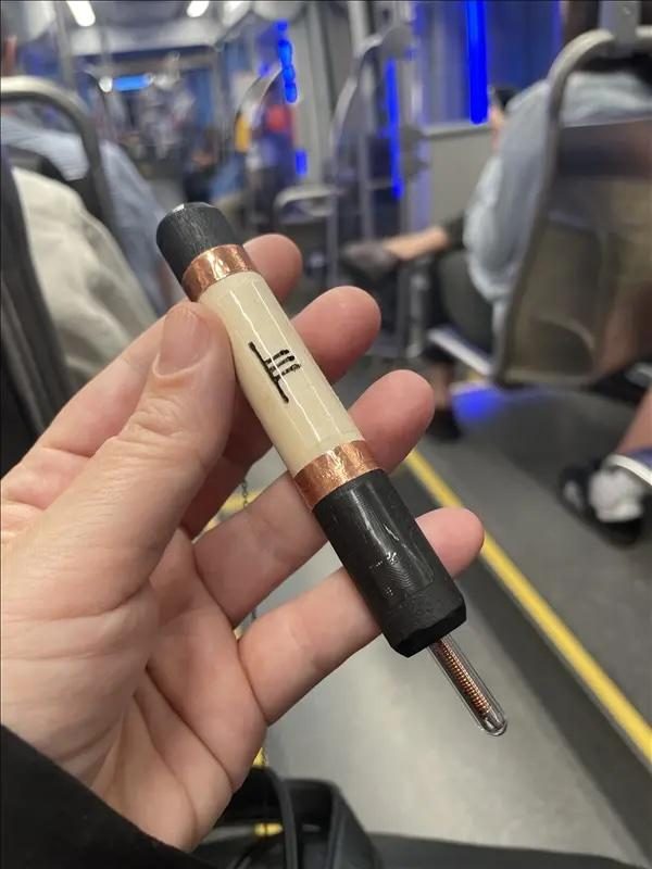 A hand holding a wooden and copper wand carved with Ogham marks, on a bus.