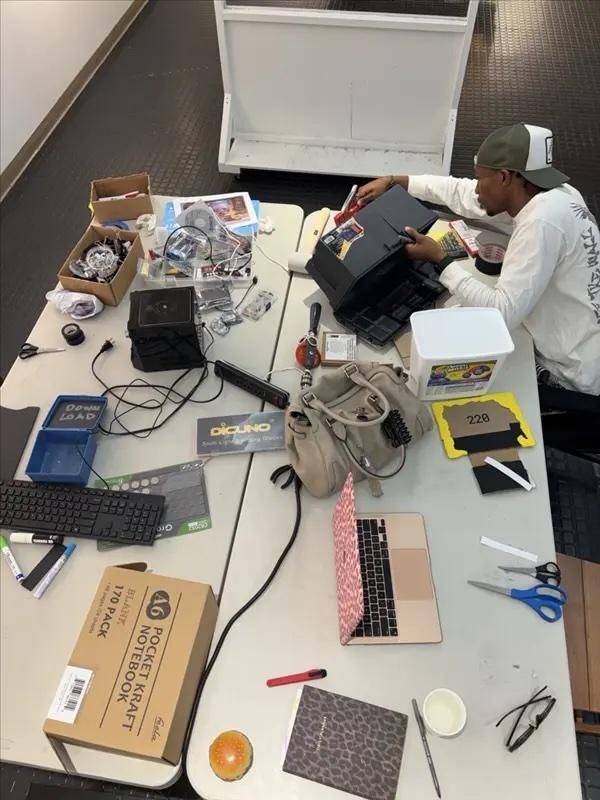 Overhead view of a workshop table strewn with components, cables, a laptop, a keyboard and a builder mid-project.