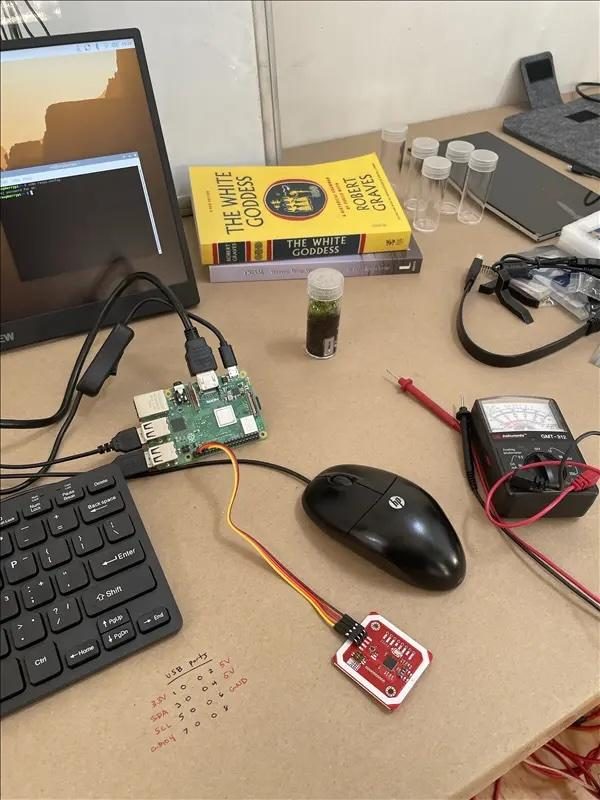 A workbench with a Raspberry Pi, a keyboard, a multimeter, a small screen, and Robert Graves's The White Goddess.