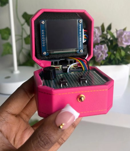 A hand holding a very small pink cyberdeck the size of a matchbox, with a tiny screen and buttons.