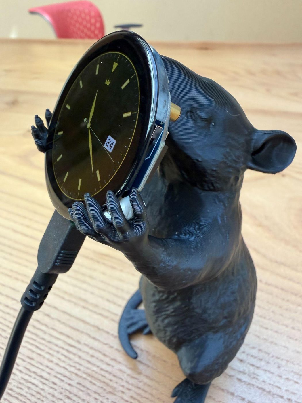 A small 3D-printed black rat standing on its hind legs, holding a large analog watch face against its chest.