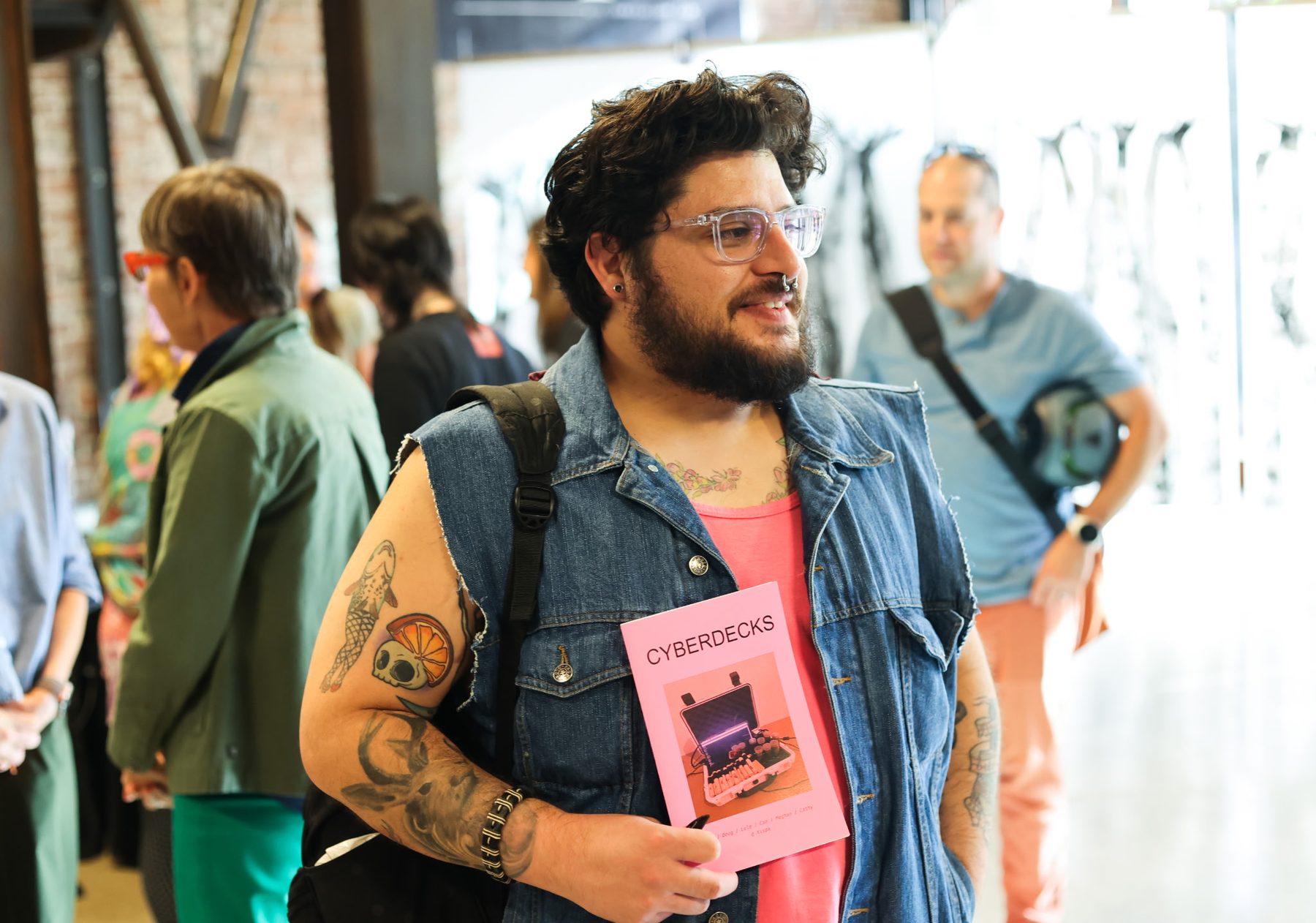 A visitor holding a pink copy of the Cyberdecks zine in the crowded space.