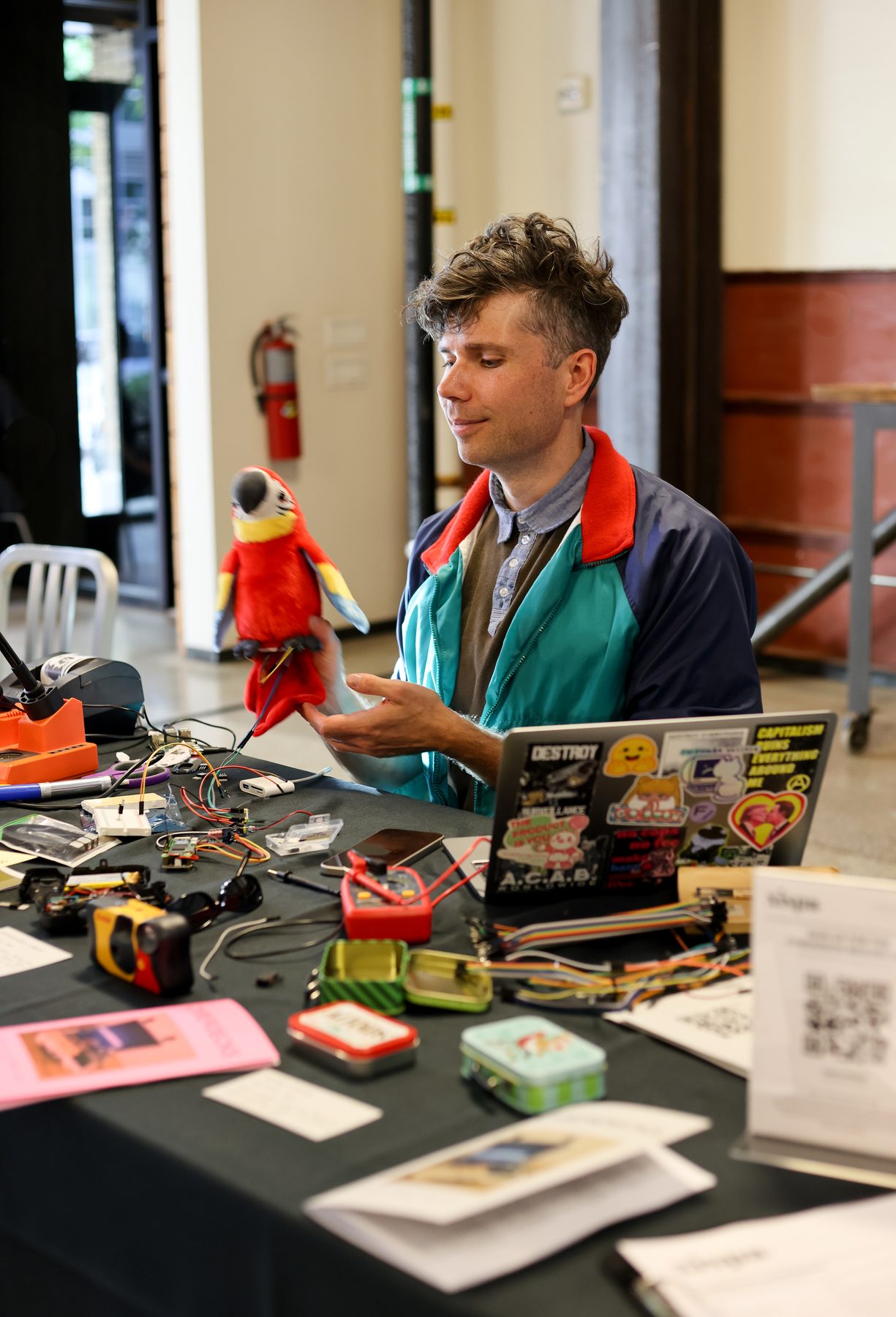 Hank Duhaime of Seattle Makers holds a red plush parrot at a table of hand-built decks.
