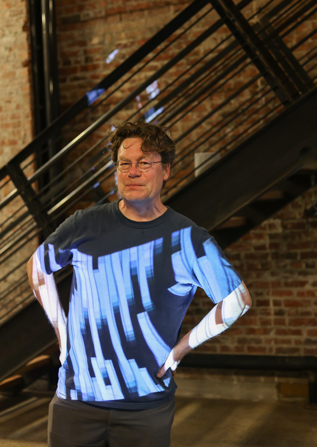A visitor wearing a shirt with a light-projected pattern, standing by an iron staircase in xispa's space.